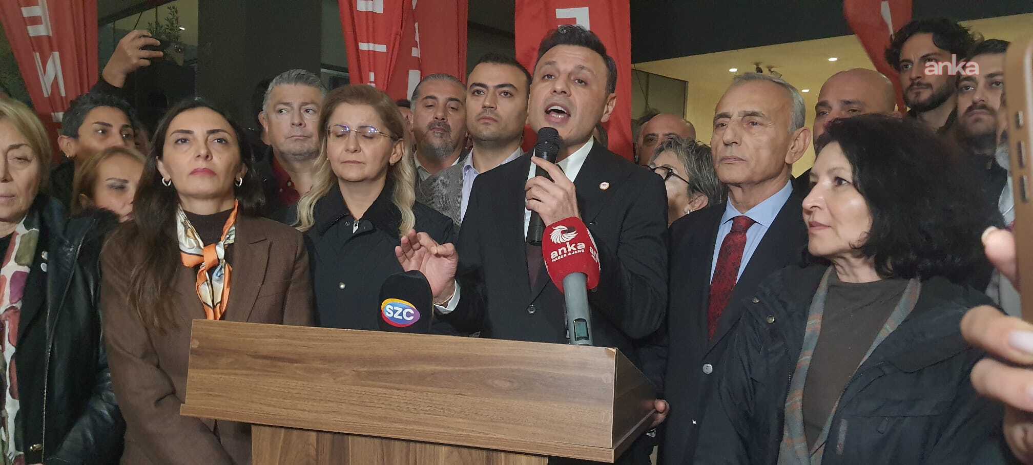 Nahaufnahme von Özgür Çelik, wie er in ein Mikrofon spricht, hinter und neben ihm befinden sich Stadtverwalter und Parteimitglieder.