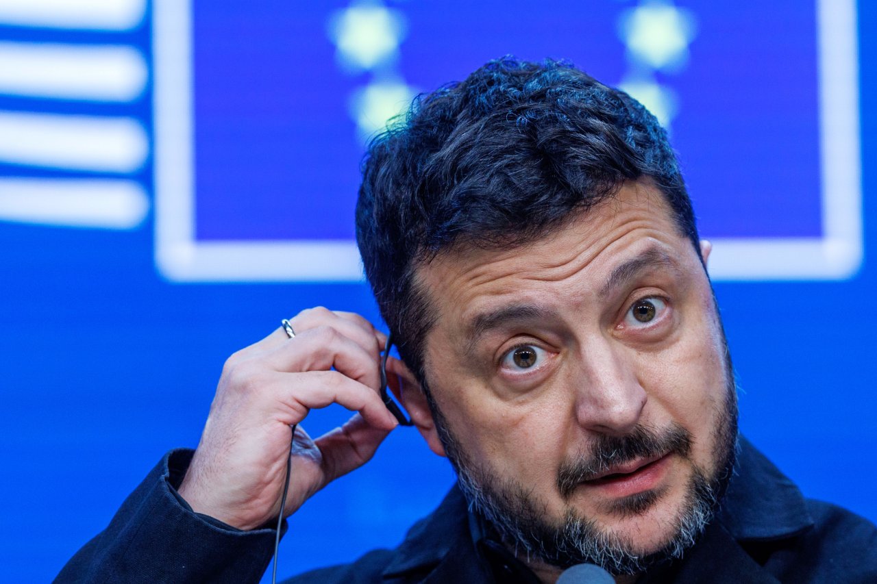 Wolodymyr Selenskyj in einer Nahaufnahme mit Kopfhörern vor blauem Hintergrund.