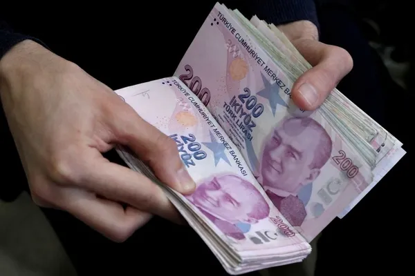Image of a person holding stacks of 200 Turkish Lira banknotes.