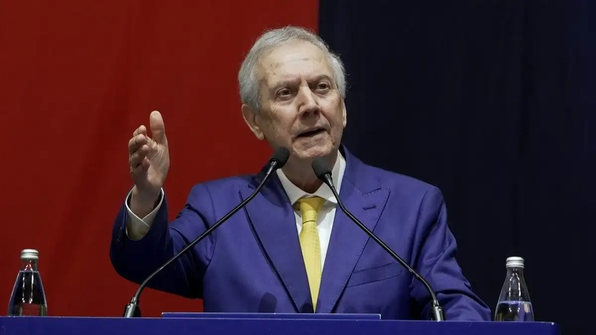 A football executive speaking in front of microphones at a podium.