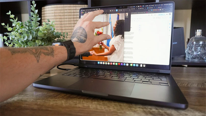 Bir kullanıcının MacBook Pro ekranındaki içerikle dokunarak etkileşim kurduğu görüntü.