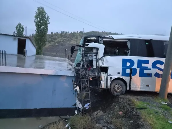 Ön kısmı hasar gören yolcu otobüsünün yol kenarındaki yapıya çarptığı kaza yeri görüntüsü.