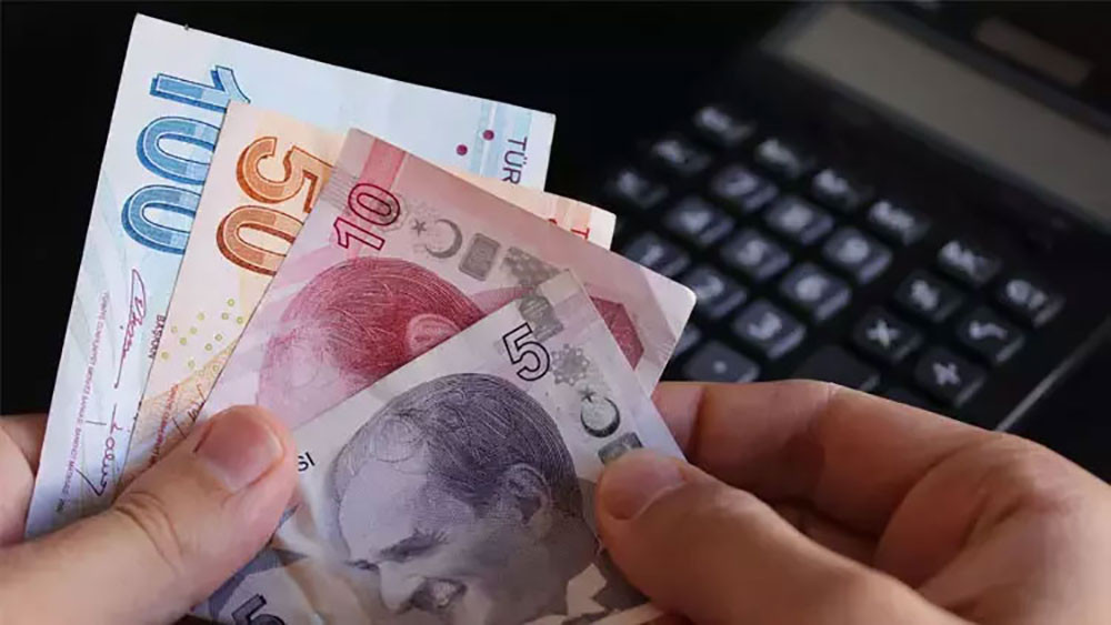 Elde tutulan Türk lirası banknotları ve arka planda hesap makinesi.