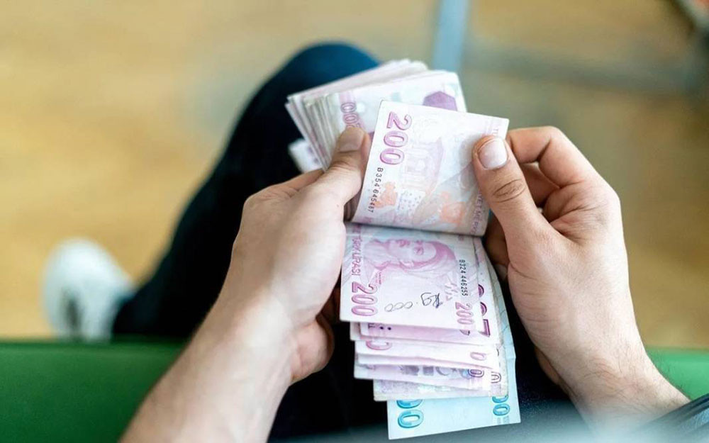 Bir kişinin otururken elinde 200 TL banknotlarını saydığı yakın plan fotoğraf.