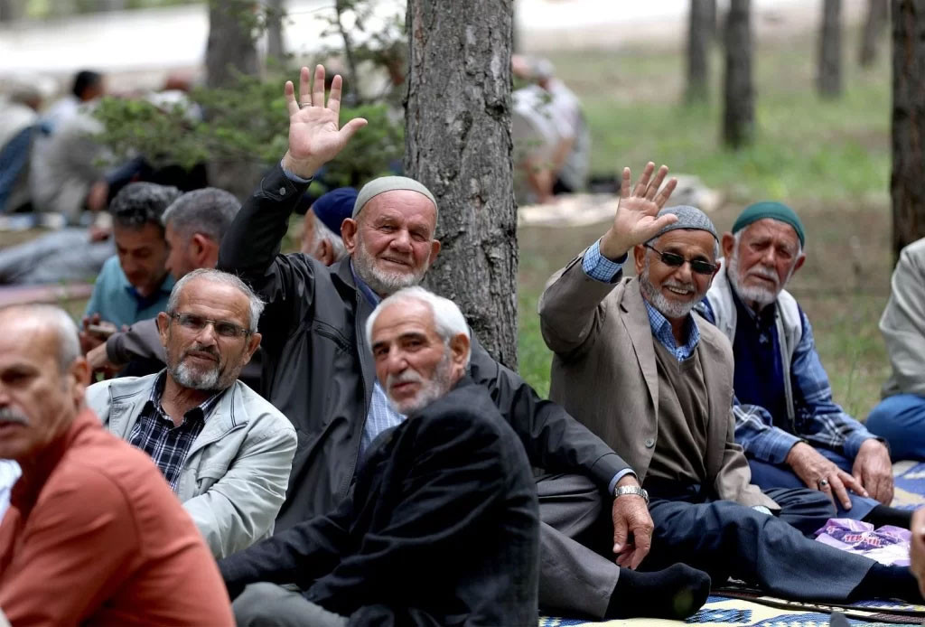 Açık alanda oturan ve el sallayan emeklilerin bulunduğu fotoğraf.