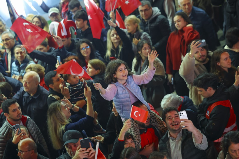 Kalabalık içinde Türk bayrağı sallayan bir çocuğun ve çevresindeki yurttaşların yer aldığı fotoğraf.