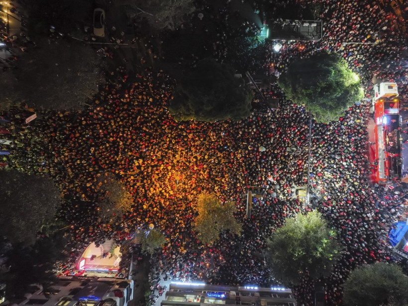 Ağaçların ve yolların arasında büyük bir kalabalığın toplandığı havadan gece görüntüsü.