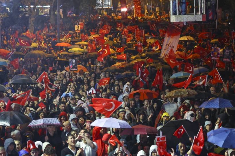Şemsiyeler ve Türk bayraklarıyla dolu kalabalık bir Cumhuriyet Bayramı kutlaması görüntüsü.