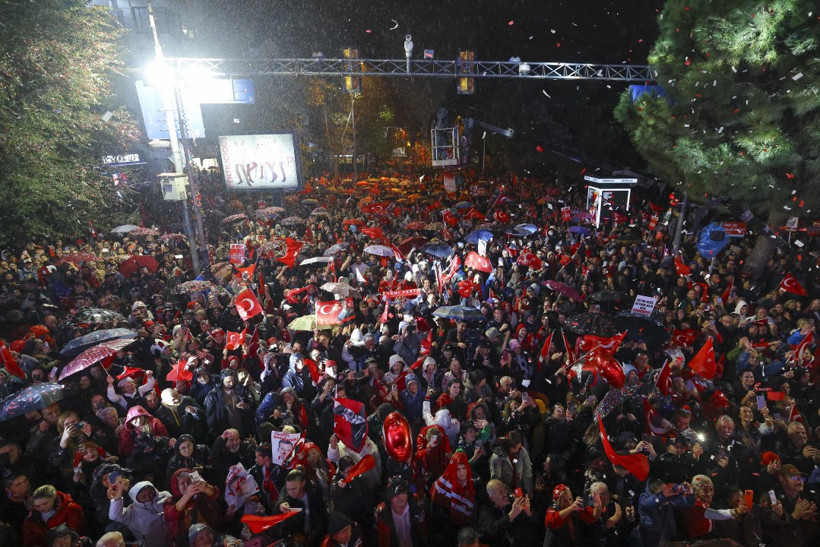 Türk bayrakları taşıyan kalabalığın gece aydınlatmaları altında toplandığı geniş açı fotoğraf.