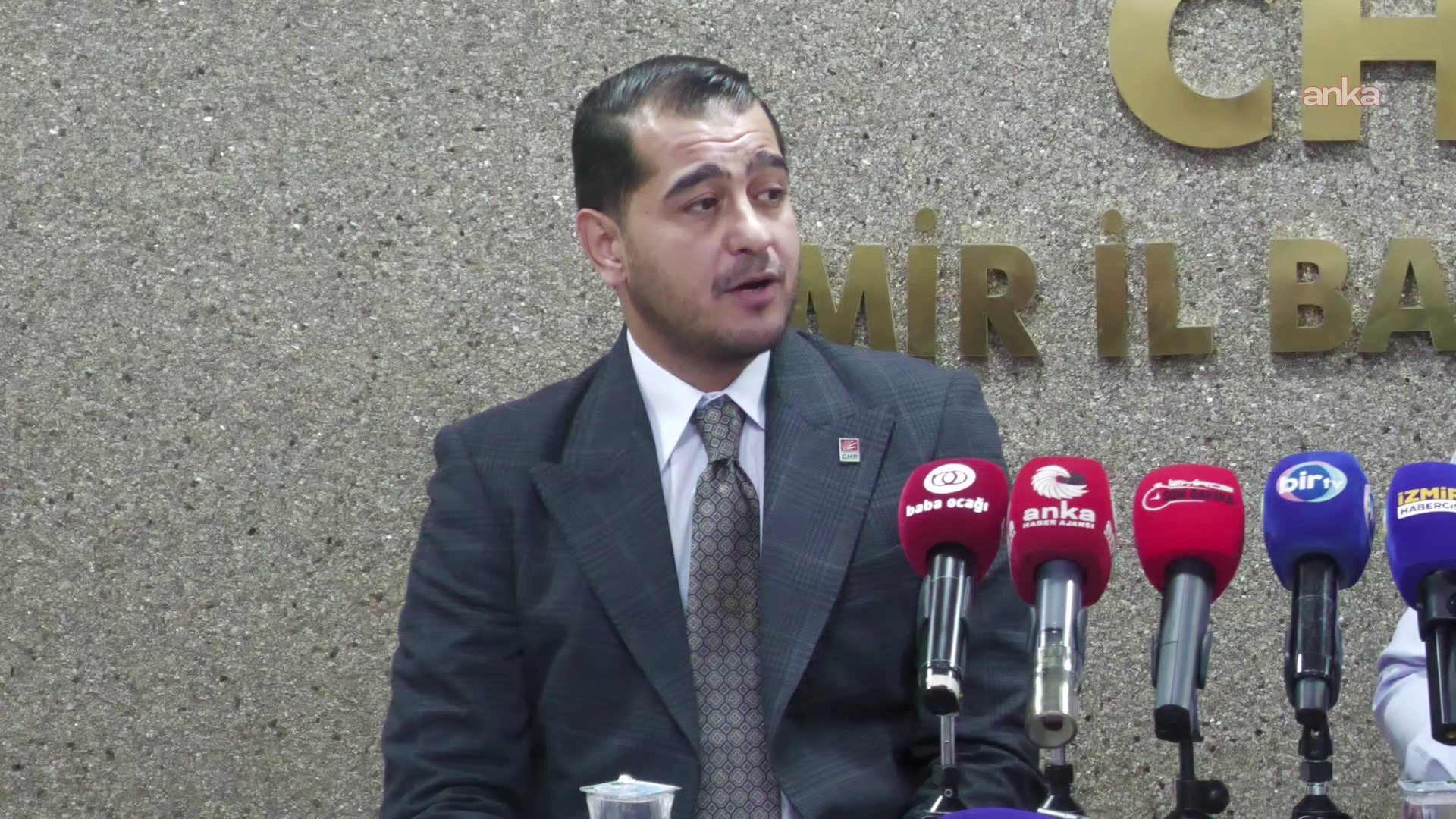 Takım elbiseli bir siyasetçinin mikrofonlar önünde konuştuğu yakın plan görüntü.