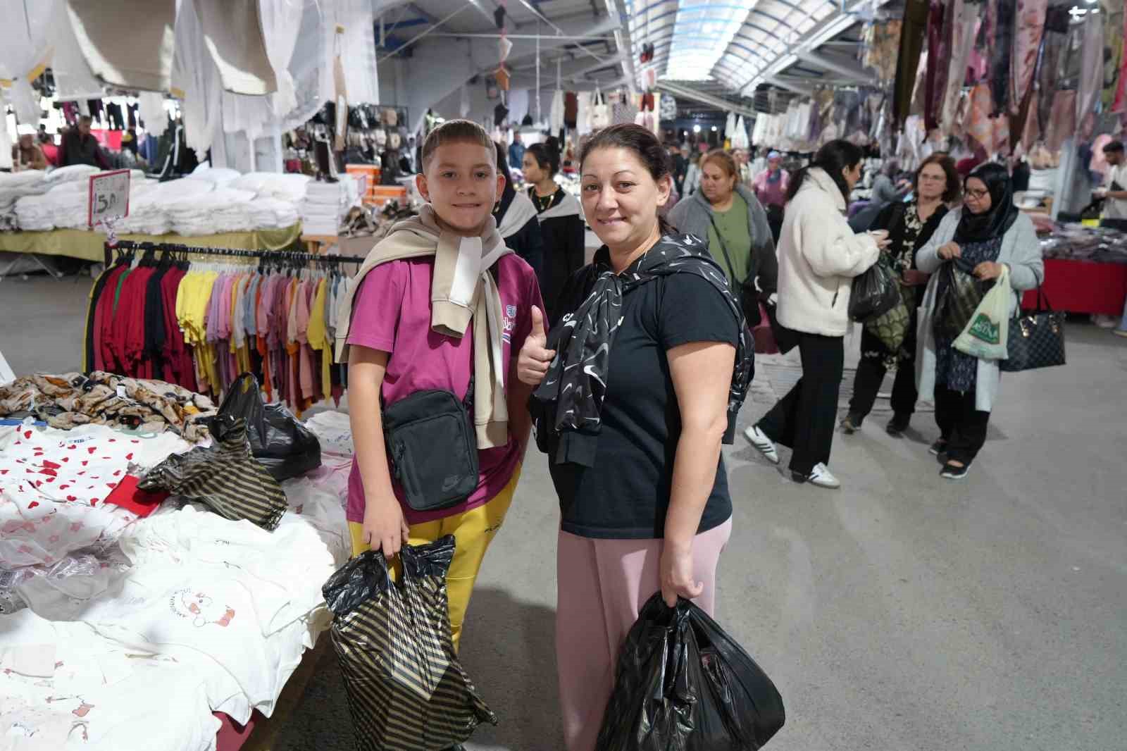 Visitatori con borse della spesa e banchi di prodotti tessili all'interno del mercato.