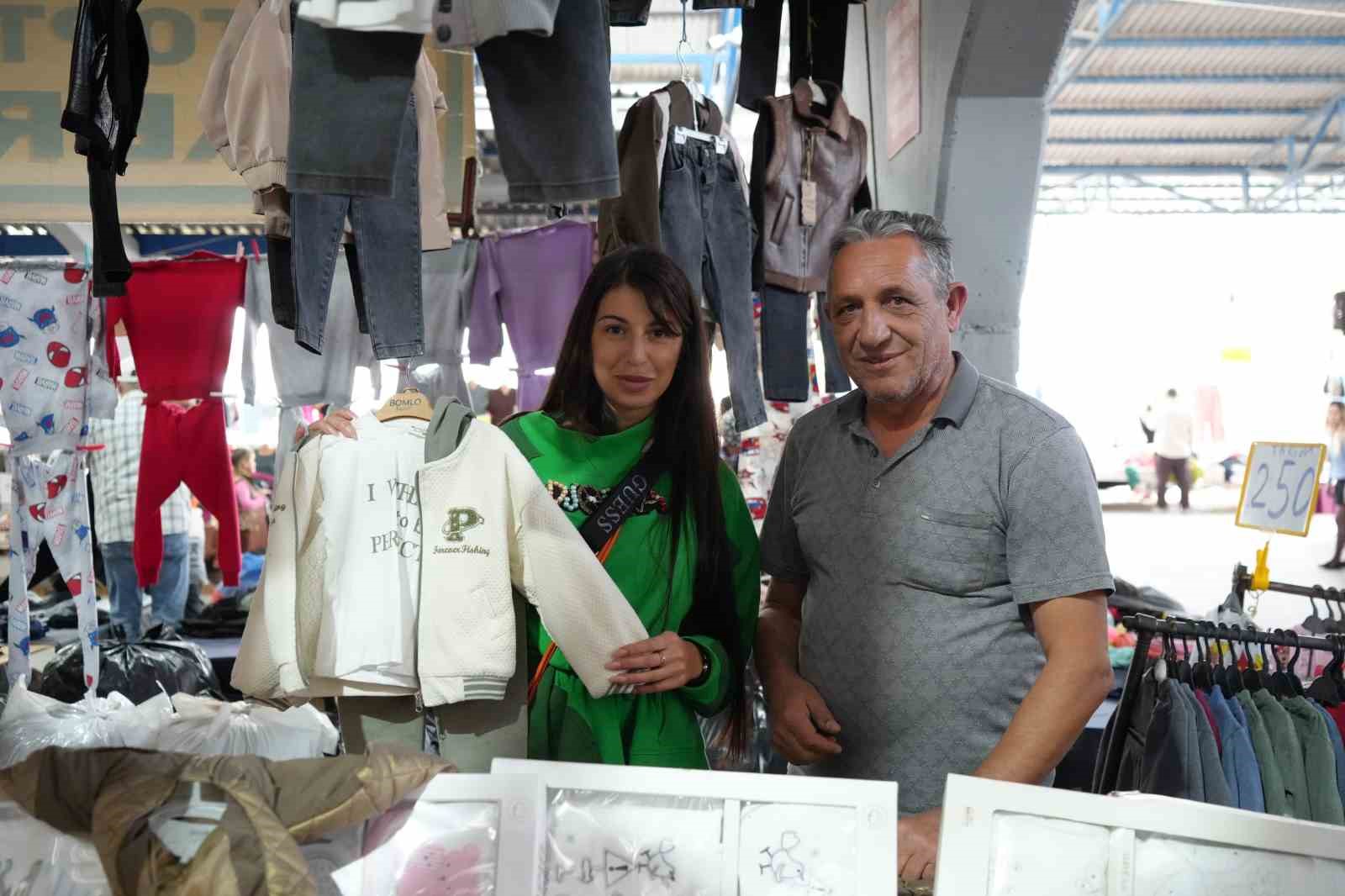 Un commerciante e un cliente presso un banco del mercato dove sono esposti capi di abbigliamento.