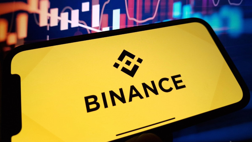 Binance logosunun yer aldığı telefon ekranı ve arka planda piyasa grafikleri