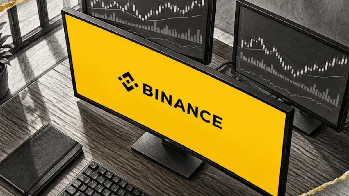 A monitor featuring the Binance logo and a desk setup with crypto market charts in the background.