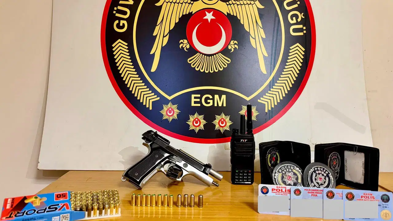 Emniyet amblemi önünde sergilenen tabanca, fişekler, telsiz, kokartlar ve polis ibareli kartlar.