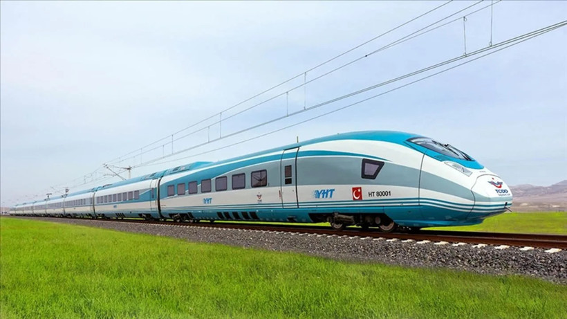 Yeşil arazi yanında elektrikli hatta ilerleyen mavi beyaz hızlı tren.
