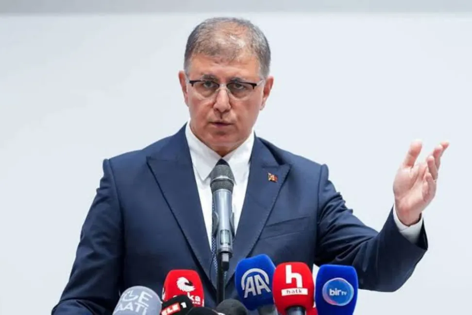 Cemil Tugay is seen speaking in front of microphones.