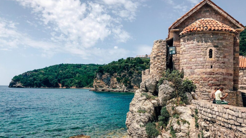 Budva kıyısında tarihi taş yapı ve deniz manzarası.