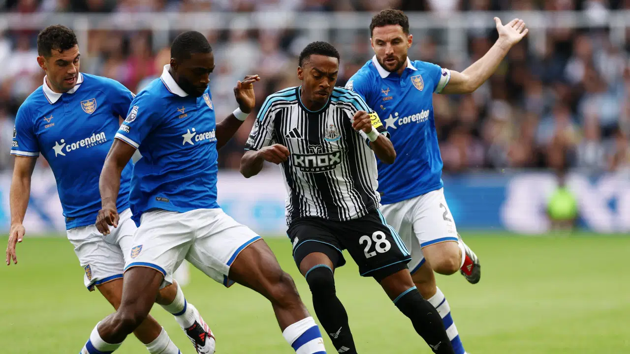 Joe Willock kontrolliert den Ball im Trikot von Newcastle United zwischen gegnerischen Spielern.