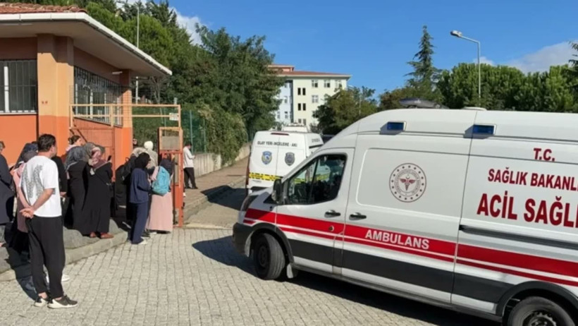 Okul girişinde bekleyen kişiler ve bir ambulans görülüyor.