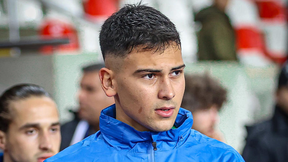 Deniz Dönmezer is seen on the sidelines wearing a blue tracksuit top.