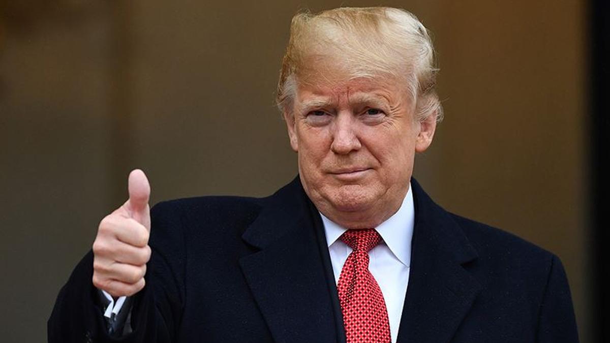 Donald Trump’ın takım elbiseyle kameraya baktığı ve başparmağını kaldırdığı bir fotoğraf.
