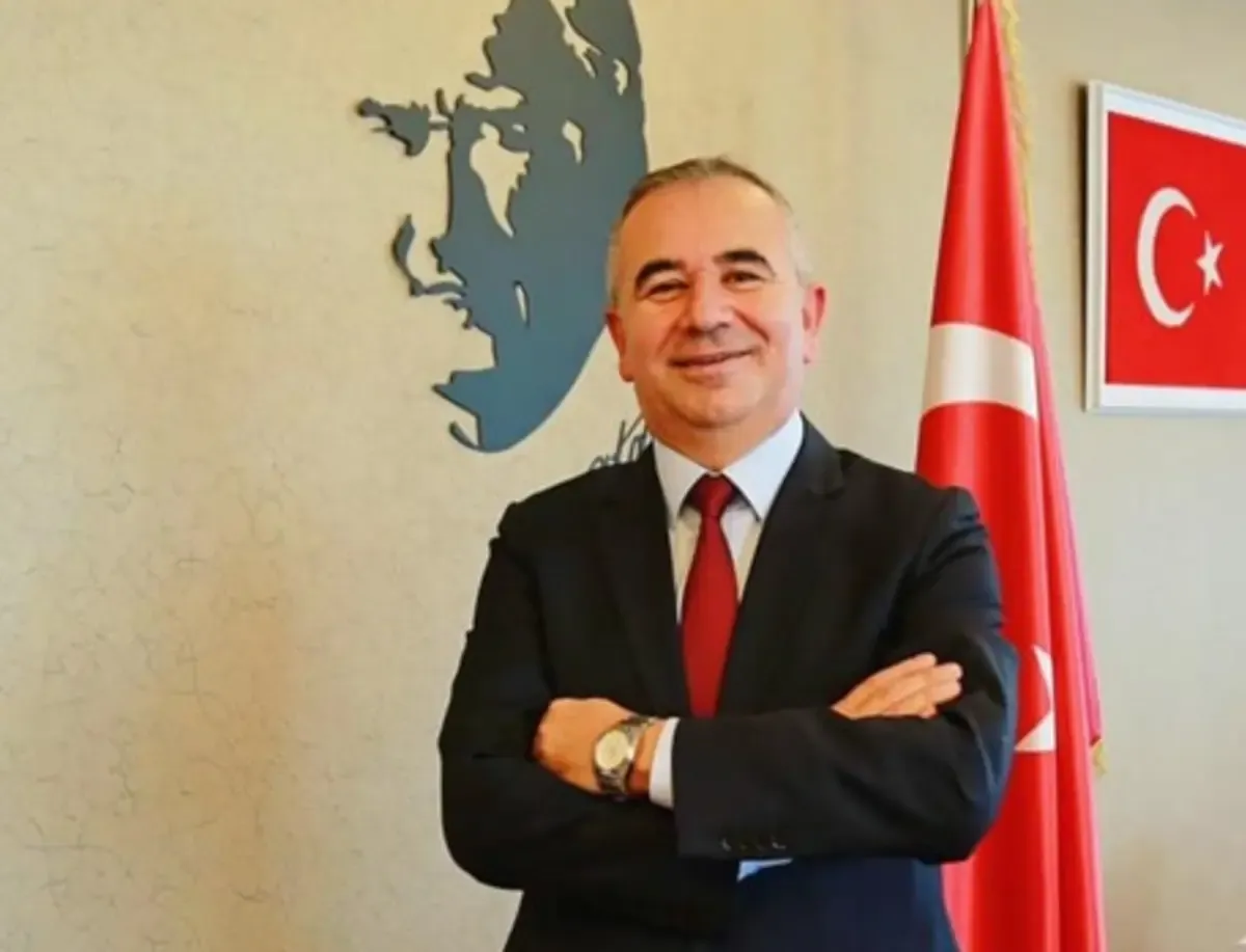 Türk bayrağı bulunan bir makam odasında takım elbiseli bir kişinin fotoğrafı.