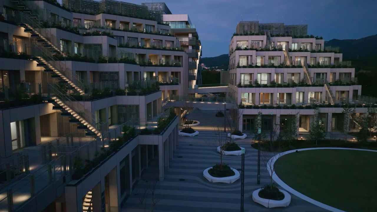 Akşam ışıklarıyla aydınlatılmış modern konaklama blokları ve avlu görünümü.