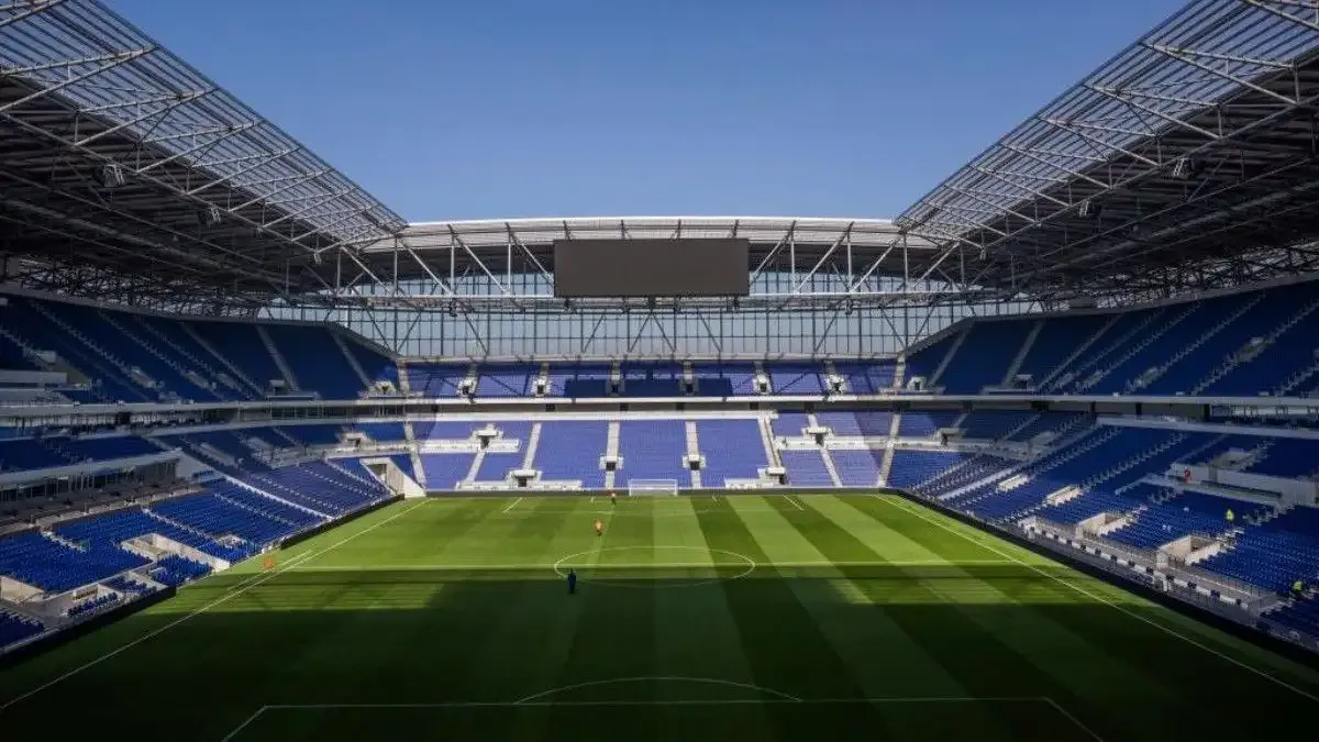 Boş tribünleri ve yeşil zemini görünen modern bir futbol stadı.