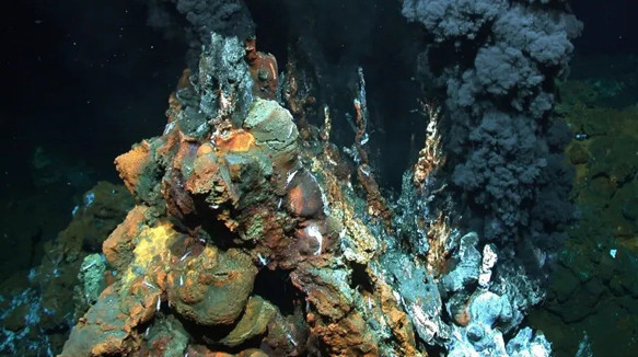 Okyanus tabanında siyah duman çıkaran hidrotermal baca ve çevresindeki mineral yapılar.