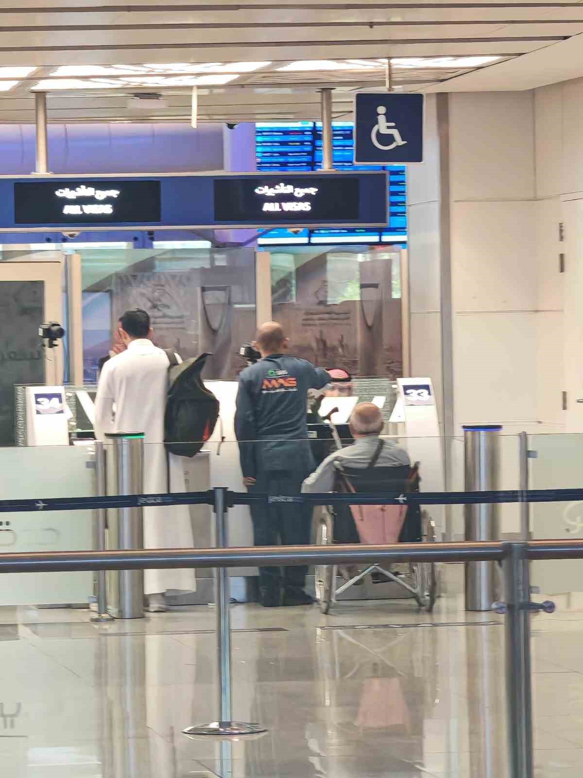 Suudi Arabistan’da bir havalimanında tekerlekli sandalyedeki Ali Baybaş ve görevliler görülüyor.