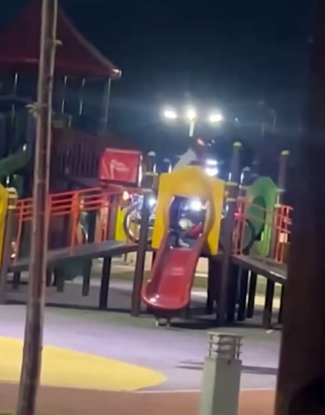 Çocuk parkındaki kaydırak ve oyun grupları çevresinde motosiklet kullanan kişi.