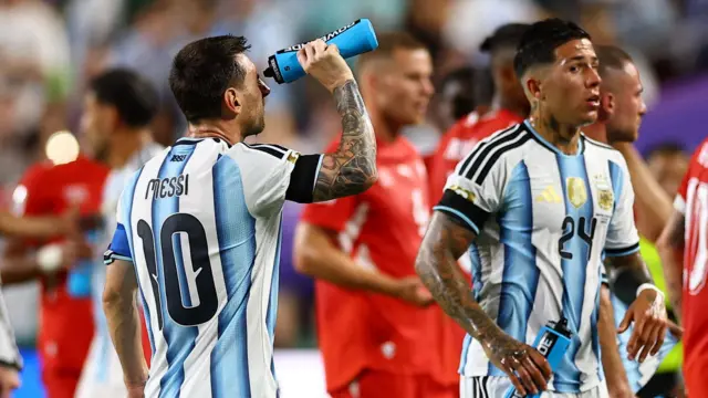 Lionel Messi, Arjantin formasıyla su molası sırasında yüzüne su döküyor; yanında Enzo Fernandez ve rakip oyuncular görülüyor.