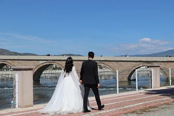 Gelinlikli kadın ve takım elbiseli erkeğin köprü üzerinde yürüdüğü temsili fotoğraf.