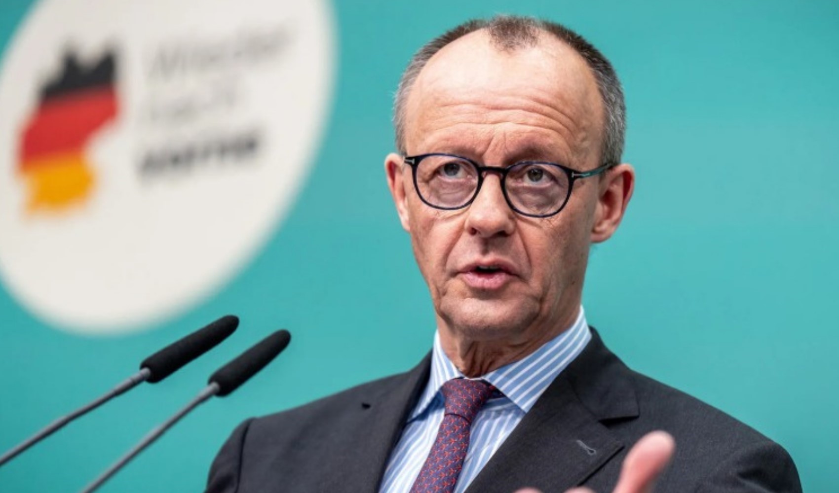 Friedrich Merz mikrofonların önünde konuşurken görülüyor.
