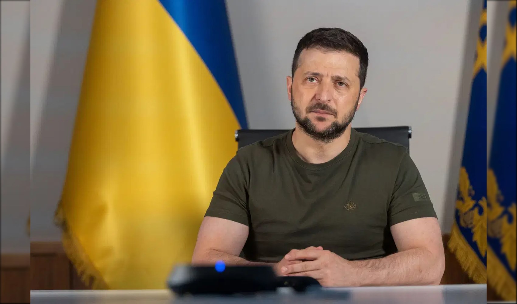 Ukrayna Devlet Başkanı Volodimir Zelenski, Ukrayna bayrağının bulunduğu bir ortamda kamera karşısında görülüyor.