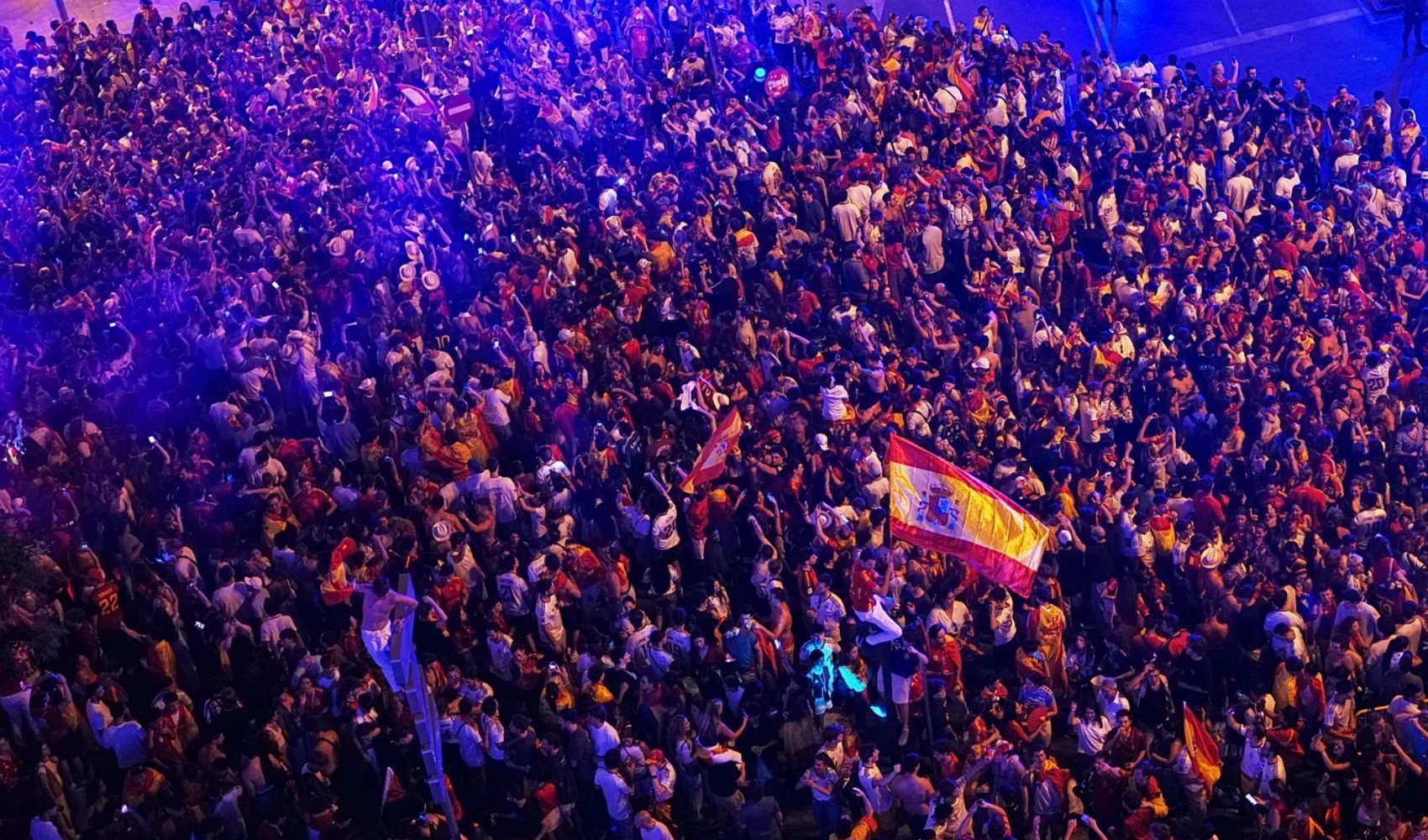 İspanya bayrakları taşıyan kalabalık bir taraftar topluluğu gece saatlerinde meydanda kutlama yapıyor.