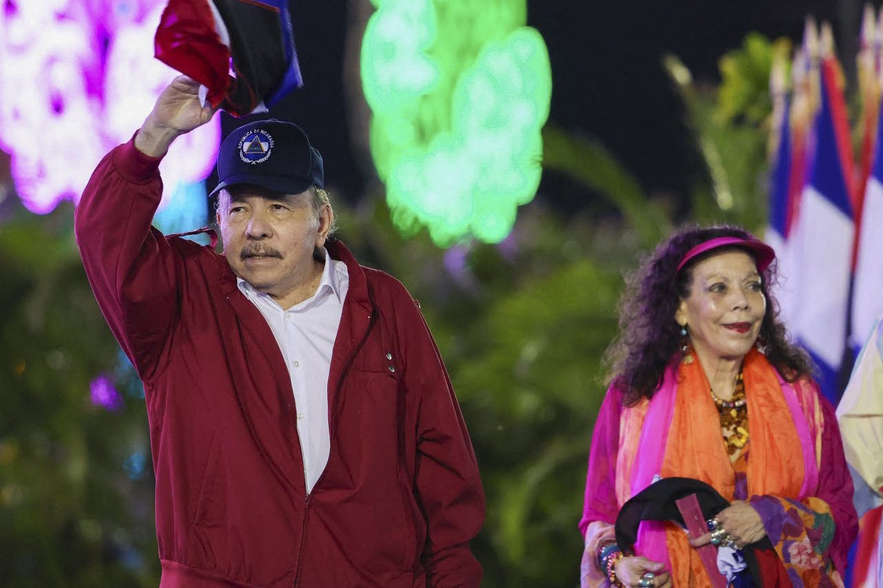 Daniel Ortega, gece düzenlenen bir törende elini kaldırırken yanında bir kadın ve Nikaragua bayrakları görülüyor.