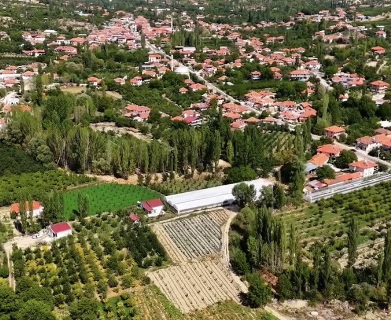 Tarım alanları, seralar ve kırmızı çatılı yerleşimlerin görüldüğü kırsal alanın havadan görünümü.