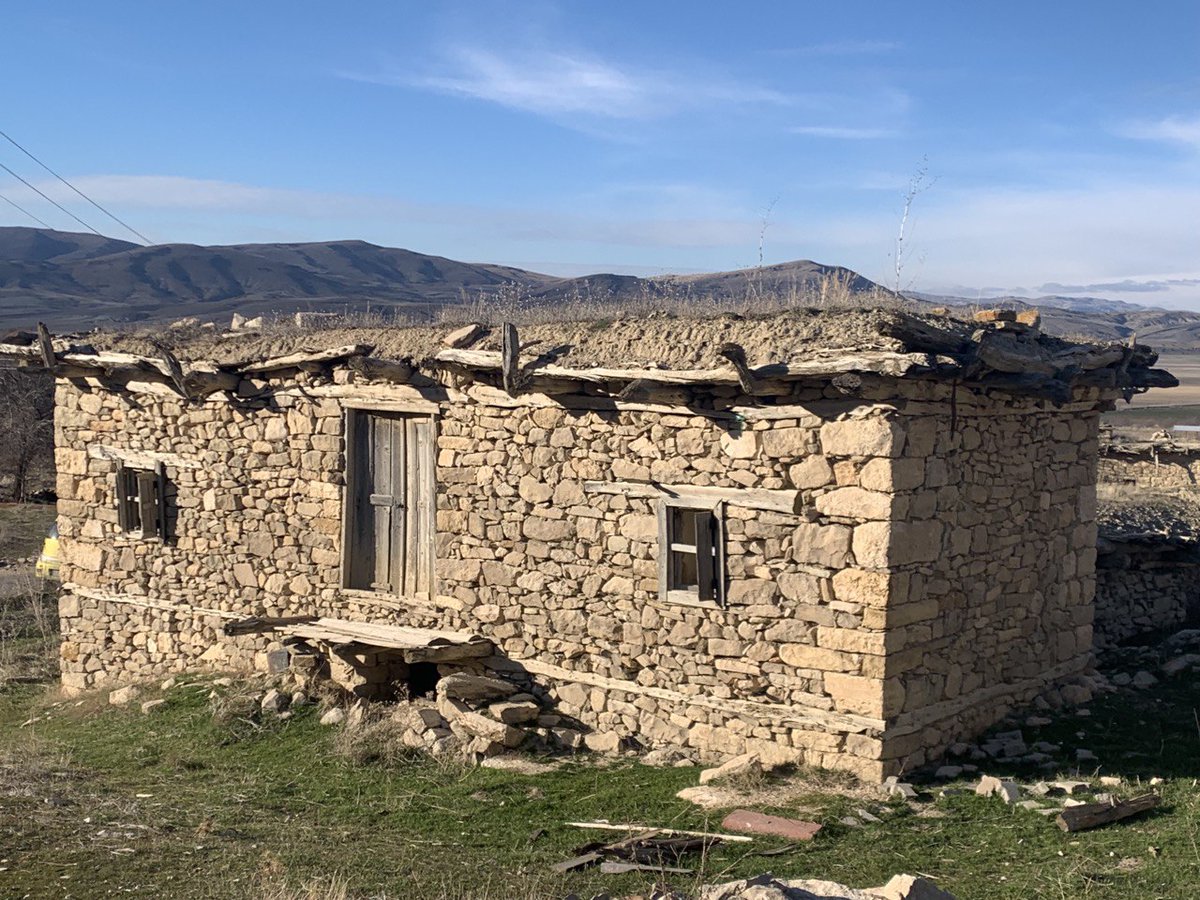 Bozkır ve dağ manzarası önünde eski taş yapı.
