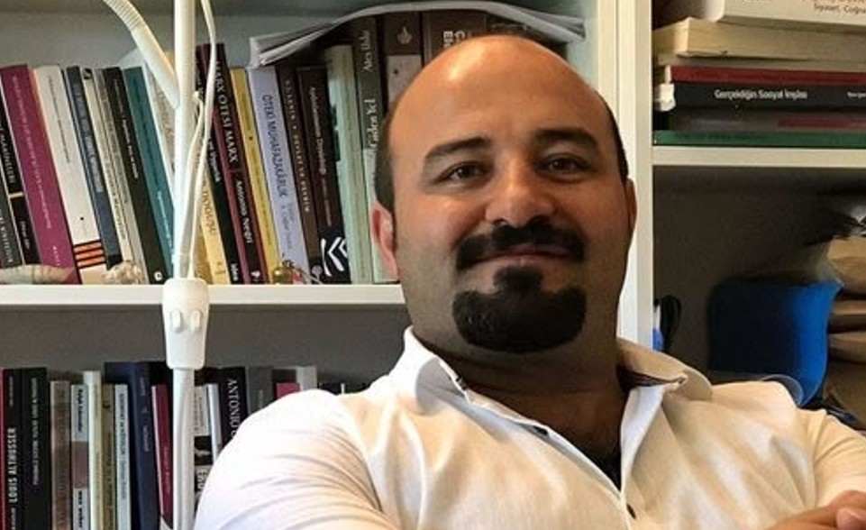 Olkan Senemoğlu’nun kitaplık önünde çekilmiş fotoğrafı.