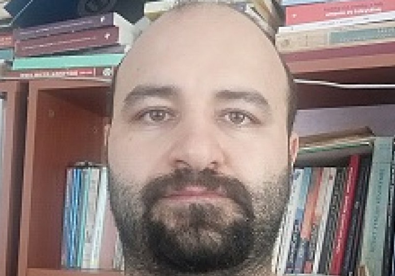 Olkan Senemoğlu’nun kitaplık önünde çekilmiş yakın plan fotoğrafı.