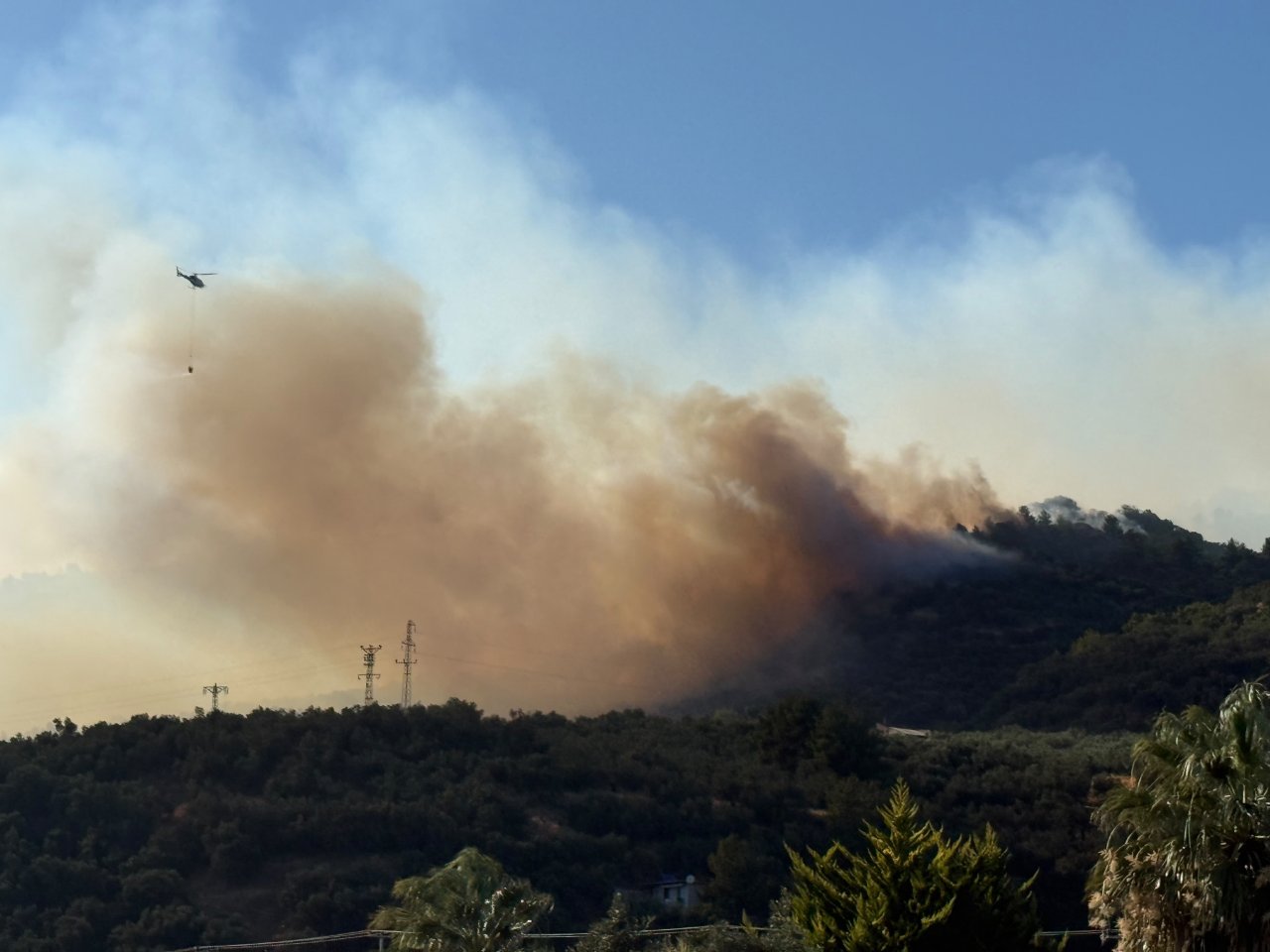 Ormanlık alanda yükselen duman ve havadan müdahale eden helikopter.
