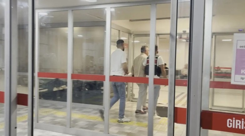 Cem Küçük’ün cam kapılı bir binanın giriş bölümünden içeri alındığı anı gösteren görüntü.