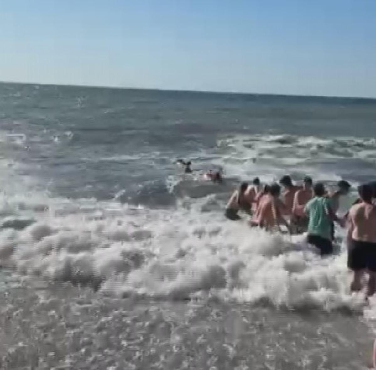 Dalgalı denizde insan zinciri oluşturan vatandaşlar.