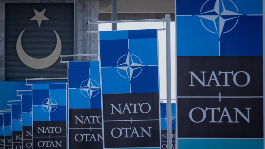 NATO tabelaları ve arka planda Türk bayrağı sembolü görülüyor.