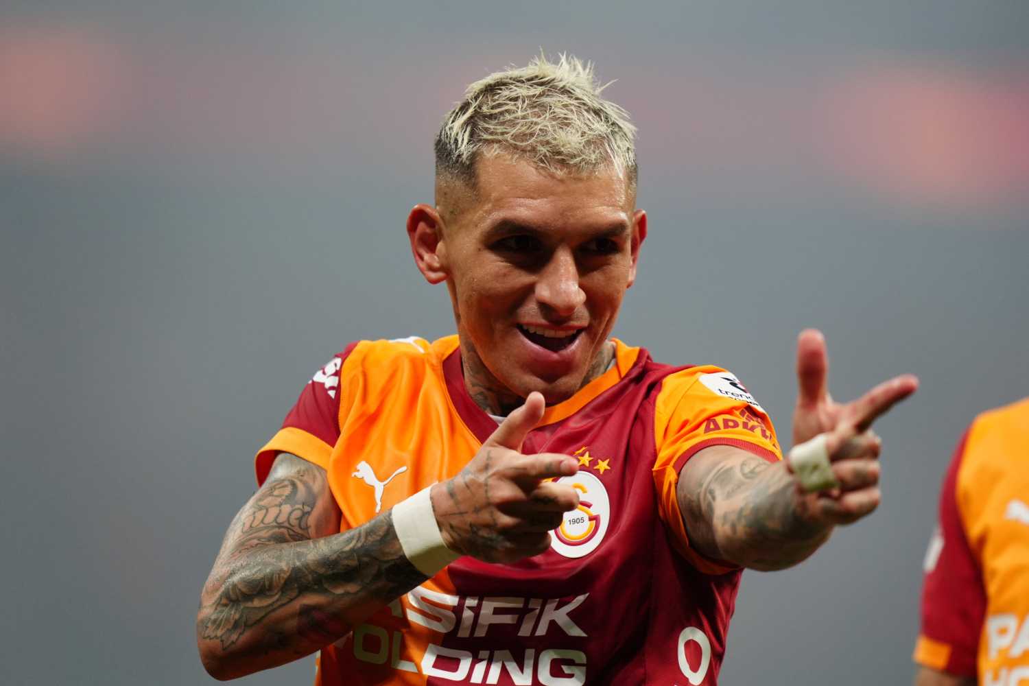 Lucas Torreira Galatasaray formasıyla gülümseyerek işaret yapıyor.