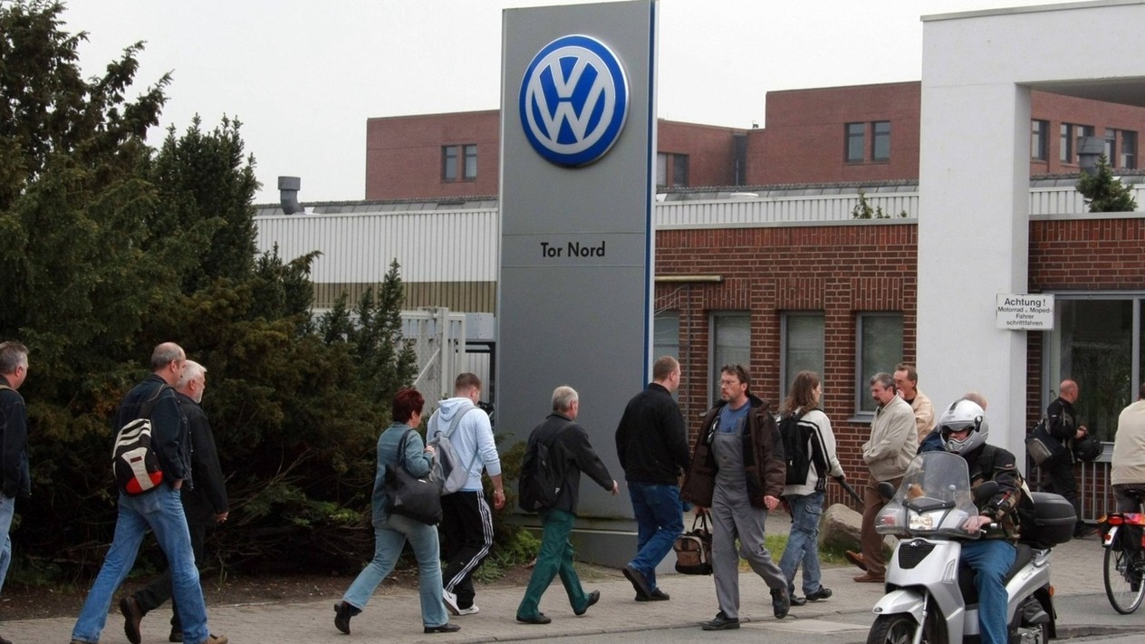 Volkswagen tesisinin girişinde yürüyen çalışanlar ve Volkswagen tabelası.