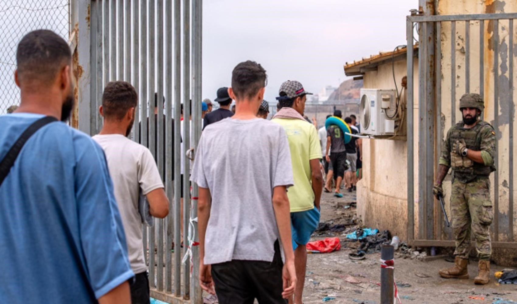 Ceuta’da bir kapıdan ilerleyen kişiler ve bölgede görev yapan bir asker görülüyor.
