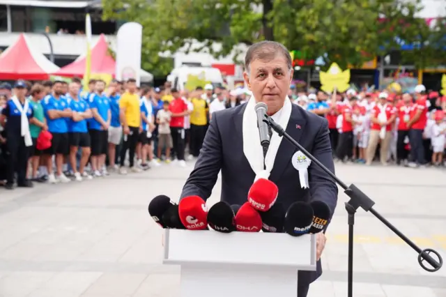 Cemil Tugay açık alanda kürsüde mikrofonların önünde konuşuyor.